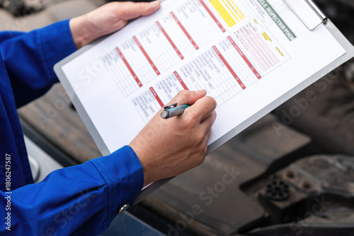 Action of a car service technician is checking on vehicle inspection checklist form during perform the maintenance job. Close-up and selective focus.