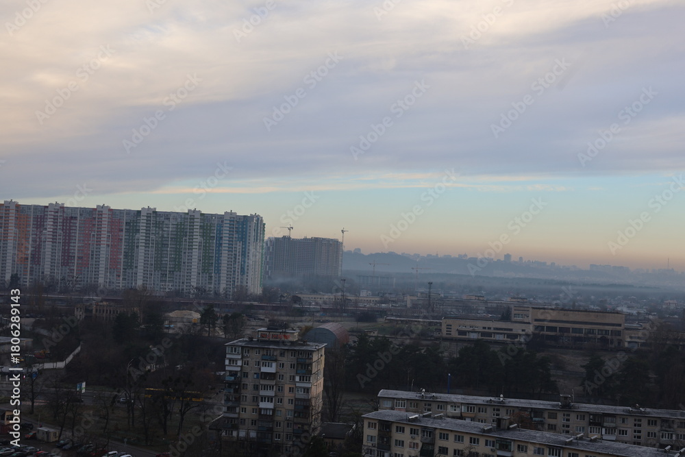 Fototapeta premium Cityscape view from high-rise building on cloudy autumn day, urban skyline with residential houses and overcast sky.