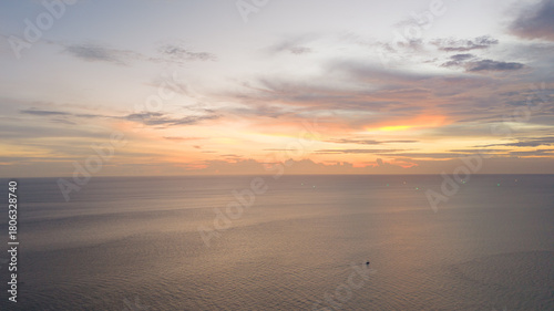 Quadro em tela Wide aerial view of a pastel sunrise or sunset over a calm ocean, highlighting a single small boat beneath a softly colored cloudscape
