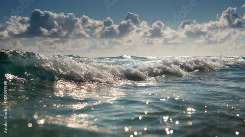 Fototapeta Naklejka Na Ścianę i Meble -  Sunlit ocean waves with sparkling clear water beneath a cloud-dotted sky