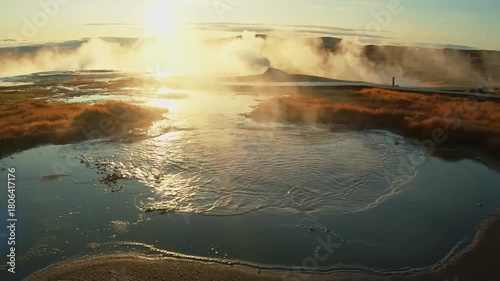 aerial shot of the Geysir geothermal area in Iceland's Golden Circle at sunrise. The footage captures the dramatic landscape as steam rises from the boiling hot springs and geysers, with the sun's ray