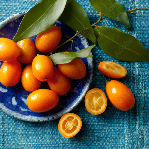 Kumquat still life, whole and sliced berries on blue ceramic plate with green leaves, top view