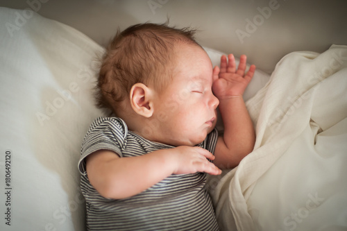 A newborn baby sleeps soundly, resting on a soft surface with a calm expression. The gentle light creates a serene atmosphere, showcasing the innocence of early life.
