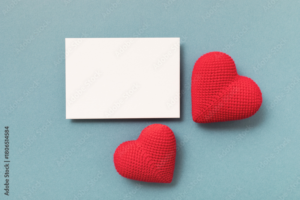 Naklejka premium Knitted red hearts and clean paper blank on blue background for Valentine day greeting card.