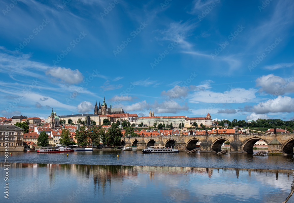Obraz premium Prague, Czech Republic, August 9, 2023. A shot with an enchanting view of the castle and cathedral dominating the hill, with the Vltava River flowing at its foot, traversed by tourist boats.