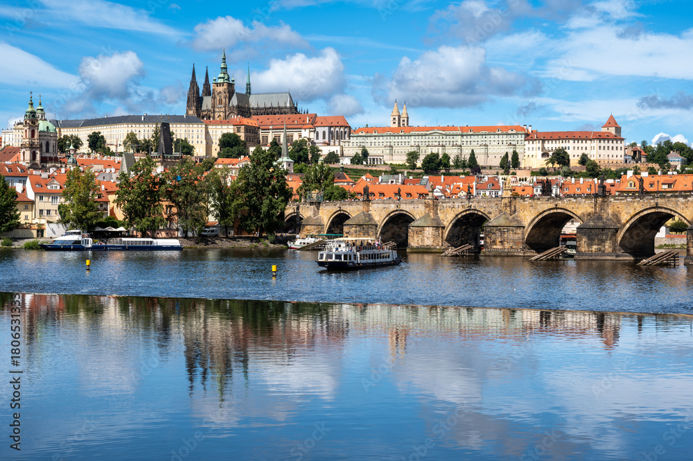 Obraz premium Prague, Czech Republic, August 9, 2023. A shot with an enchanting view of the castle and cathedral dominating the hill, with the Vltava River flowing at its foot, traversed by tourist boats.