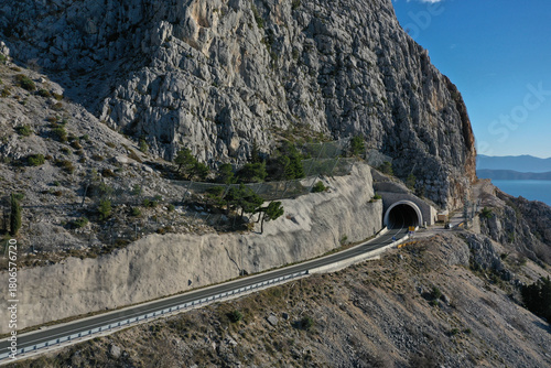 Aerial view of a road disappearing into the dark mouth of a tunnel carved into the stark, rocky mountainside, Split-Dalmatia County, Croatia.
