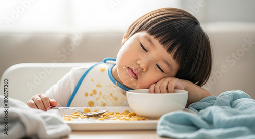 Toddler in bib with food stains, sleepy expression at breakfast table, childhood nurture and morning routine
