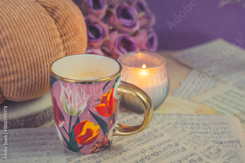 Warm latte in floral cup with candlelight and knitted textures, cozy autumn mood