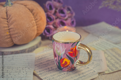 Warm latte in floral cup with candlelight and knitted textures, cozy autumn mood