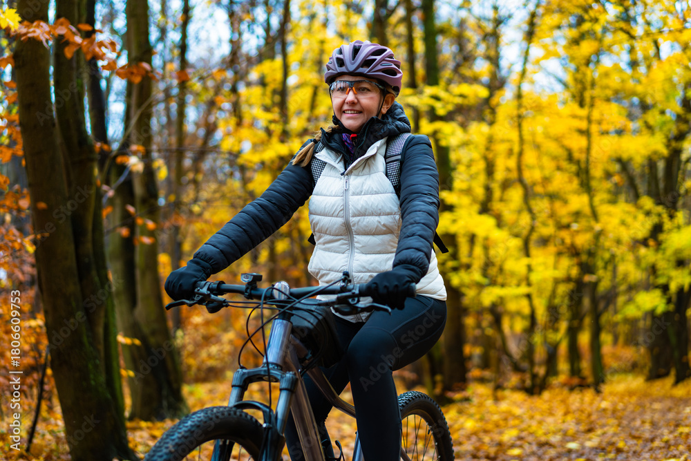 Fototapeta premium Beautiful middle-aged woman riding bicycle in forest in autumn. Front view 
