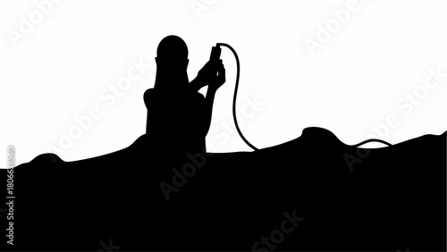 Silhouette of person holding a device with a cable against a white background and dark landscape