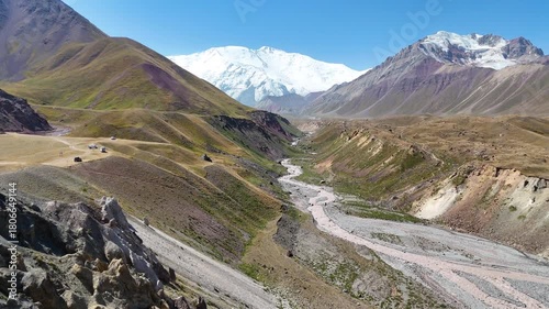 This aerial video reveals the breathtaking scenery of the Alay Valley in Kyrgyzstan, where the majestic Lenin Peak rises above the Chon-Alay mountain range under a clear sky.