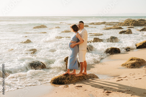 Couple embracing on beach rock as waves crash behind