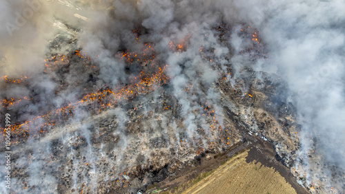 Aerial view of a raging fire consuming a vast field, smoke billowing into the sky, contrasting with the untouched golden field nearby, Osijek, Osijek-Baranja County, Croatia.