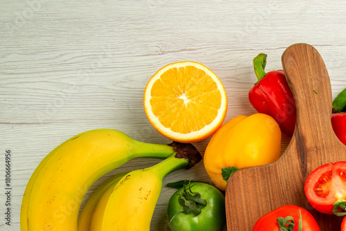 Fresh fruit and vegetables including bananas, orange, and bell peppers on wood backdrop