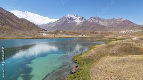 Drone captures Tulpar-Kul Lake’s stunning turquoise-blue waters in Kyrgyzstan. Traditional yurts sit along the shore, while the majestic Lenin Peak.