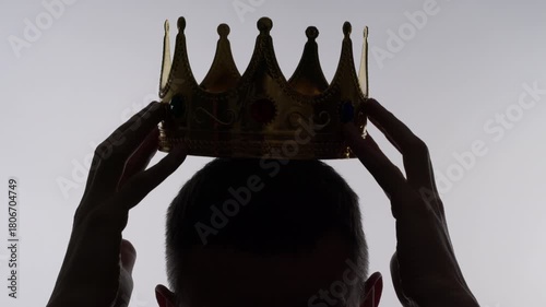 A silhouette of a man placing a crown on his head. Concept of greatness and leadership.
