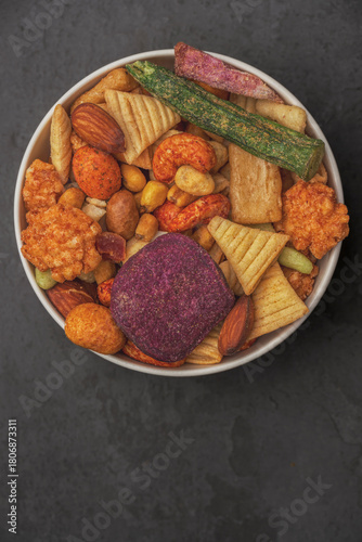 A bowl of assorted snacks including nuts, raisins, and potato chips.