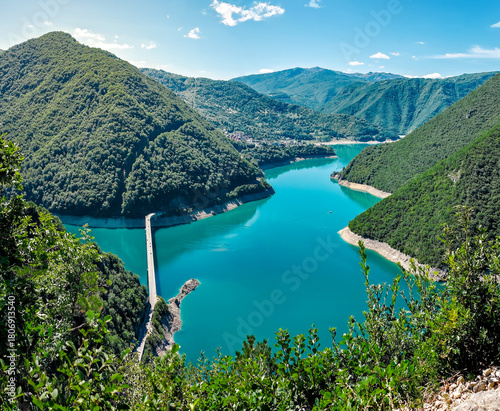 Panoramic view of Piva Lake and its winding shoreline in Durmitor National Park, Montenegro. Verdant green mountains rise above the calm turquoise water, with a narrow bridge crossing the canyon below