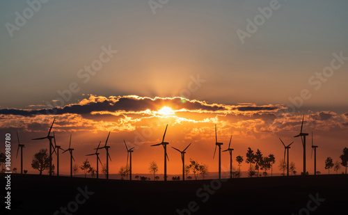 Wind turbines on the horizon during sunset, landscape with trees and shrubs. Energy, environment, wind power, sustainable energy.