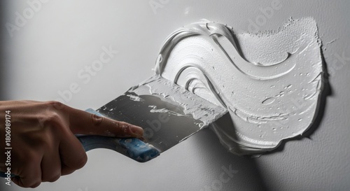 Hand with putty knife applying plaster on white wall Construction repair concept.