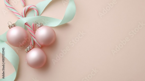 Flat lay of pastel pink baubles and mint ribbon with candy canes on pale peach background for festive decor