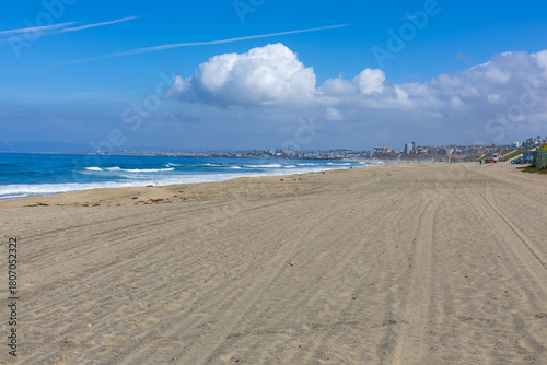 Redondo Beach coastline with waves, sand, and residential houses under a blue sky.