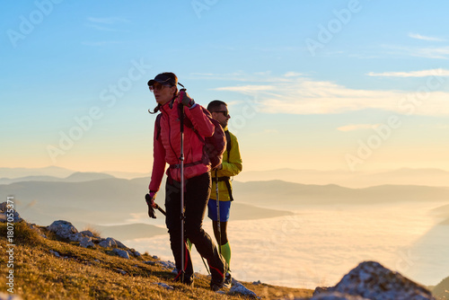 Couple exploring stunning mountain landscape during early morning sunrise with clouds below