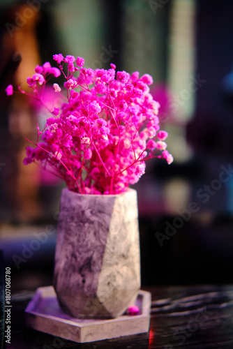 Bright pink flowers arranged in stone marble vase placed on a dark table against blurred background