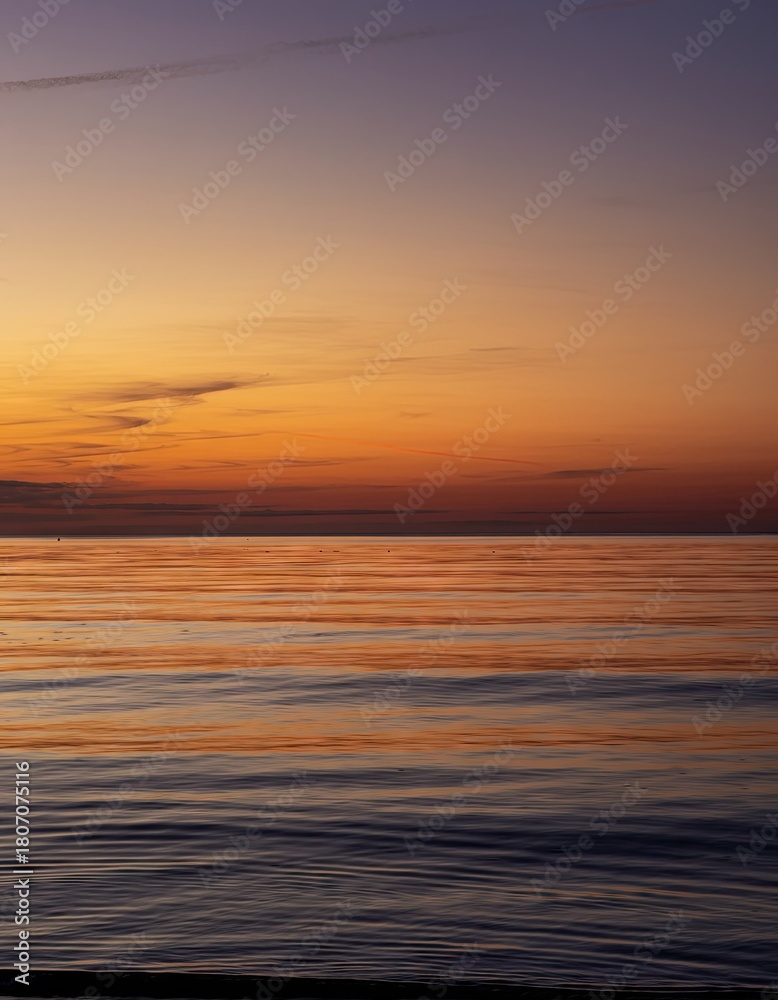 Obraz premium Vibrant orange and purple sunset sky reflects on calm ocean water with distant birds flying in a peaceful twilight scene