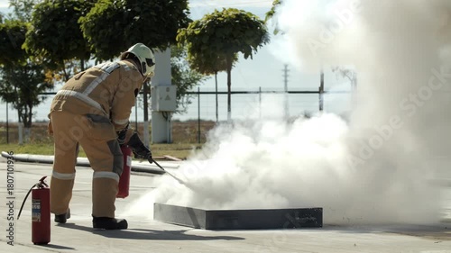 Firefighter extinguishing training fire with extinguisher outdoors