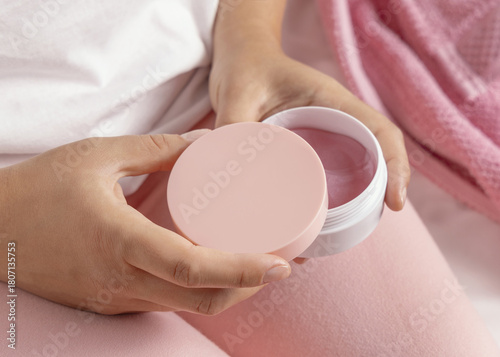 Closeup of woman in pink pyjamas holding cosmetic jar with blank lid in hands, mockup