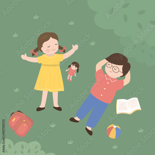 Top view of cute girl and boy lying down on green lawn. Little friends lying on grass dreamily. Various items near kids - ball, doll, backpack and book.