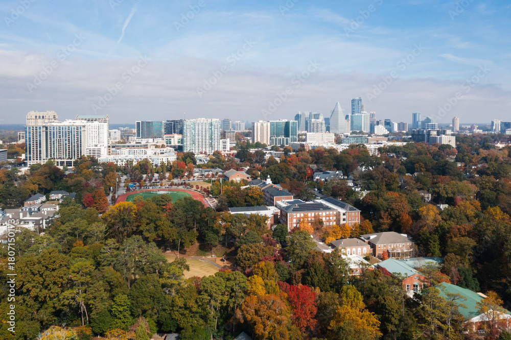 Obraz premium Aerial view of a modern city skyline overlooking a residential neighborhood filled with vibrant autumn trees.