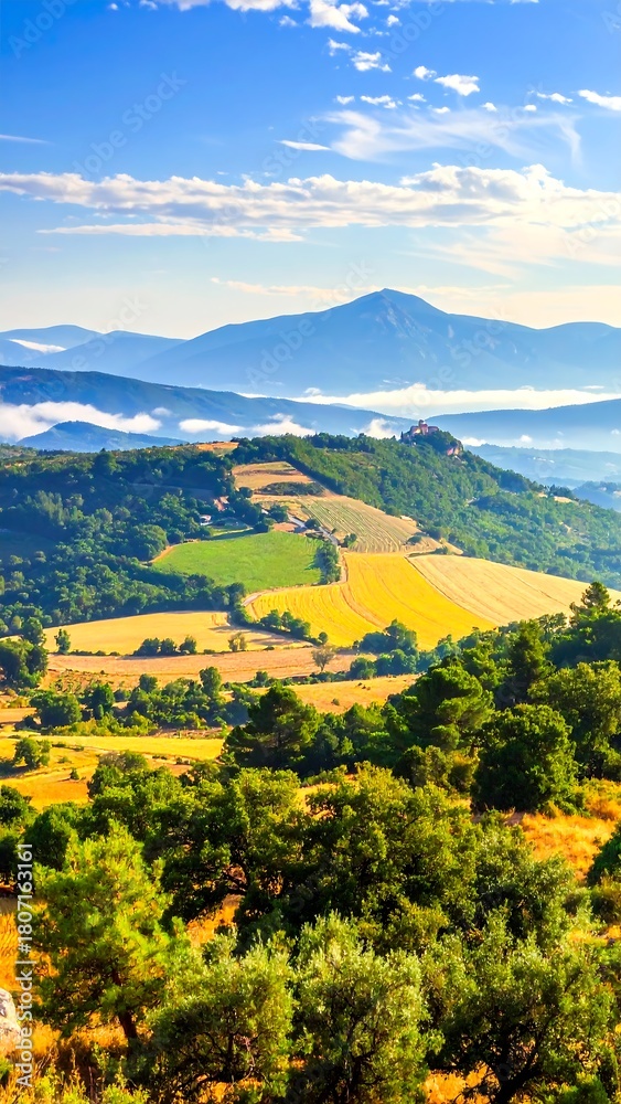 Naklejka premium Lush green and golden fields sprawl across rolling hills beneath a vast blue sky.