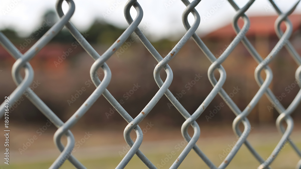Fototapeta premium Close up of a weathered chain link fence with blurred outdoor background suggesting confinement or division