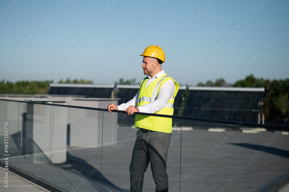 Obraz premium Technician in safety vest standing near solar panel field