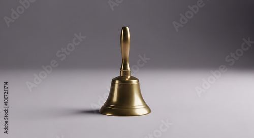 A shiny brass handbell with a long handle sits on a light surface against a gray background