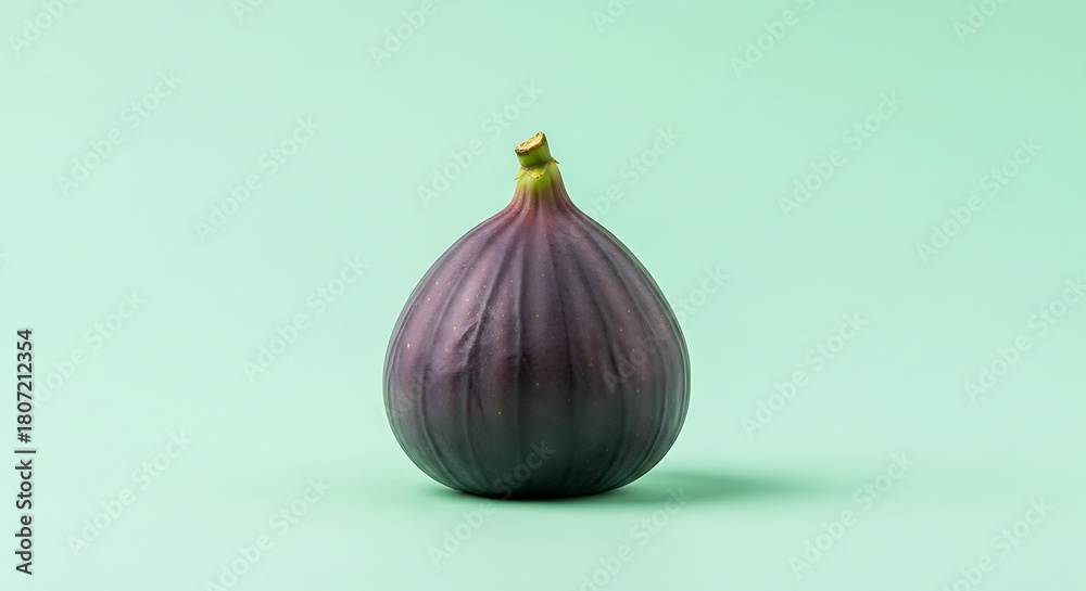 Fototapeta premium A single ripe fig centered on a light green background with a soft shadow underneath it in studio light