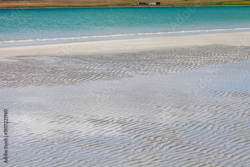 blue green shimmering sea and pale golden sand lit by summer sunshine on a beach on the island of Stronsay in Orkney, Scotland, UK