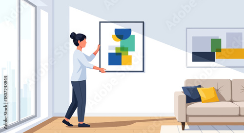 A woman adjusts a framed artwork in a sunlit living room with a sofa and another artwork on the wall