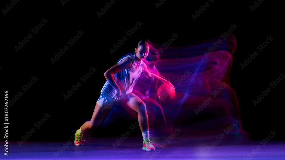 Naklejka premium Female basketball player dribbling with ball in glowing studio motion. Concept of fitness promotion, motivation visuals, sports branding, and energetic lifestyle ads.