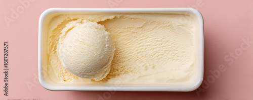 Creamy vanilla ice cream scooped from a carton, placed on a soft pink background showcasing its smooth texture