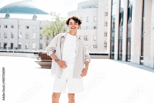 Portrait of young attractive man with curly hair hairstyle. Smiling handsome male in casual stylish clothes posing in the street at sunny day. Cheerful and happy model outdoors