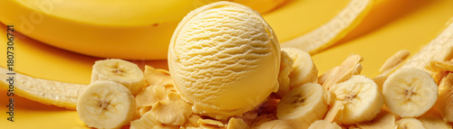 Banana ice cream scoop surrounded by fresh banana slices and banana peels on a vibrant yellow background