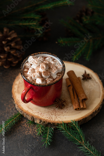 Hot chocolate with marshmallows in a red mug on a festive background with pine branches and cones for Christmas and winter holidays