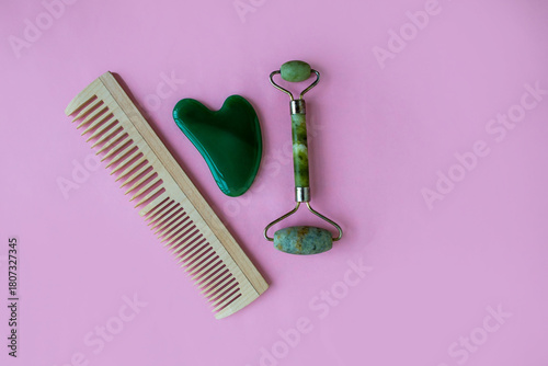 Jade massager and hairbrush on a pink background. Background with copy space.