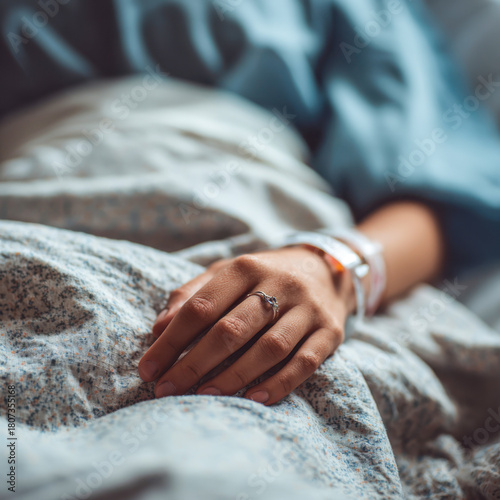 close-up of a patient’s hand resting on a hospital bed, adorned with medical bracelets and a ring, evoking feelings of vulnerability, care, and quiet resilience