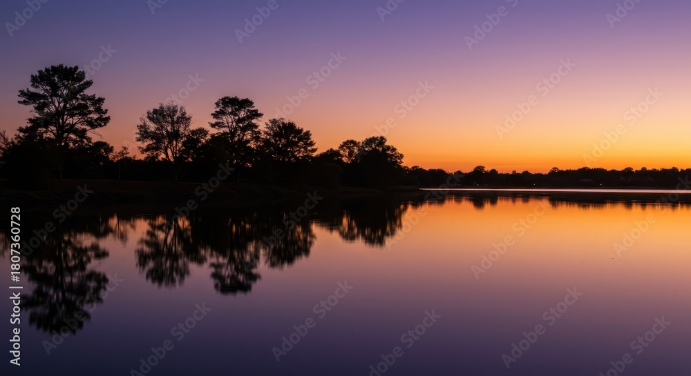 Obraz premium Tranquil water reflects colorful twilight sky behind silhouetted trees along the horizon
